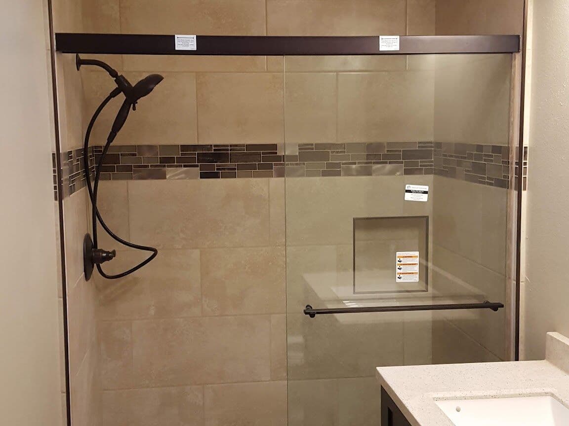Bathroom with wood-look porcelain floor, tiled shower with a glass mosaic band and a glass shower door