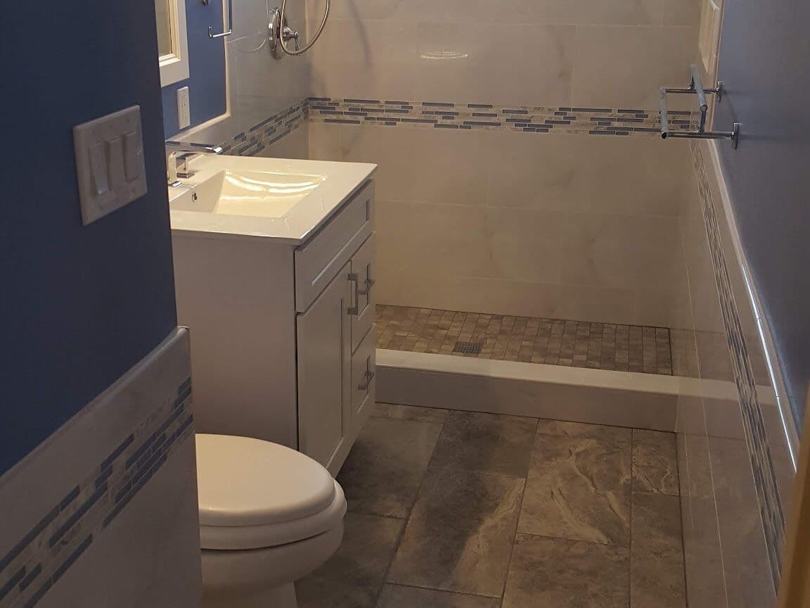 Remodeled bathroom with navy walls, white large-format shower tile, a blue glass mosaic band and new vanity