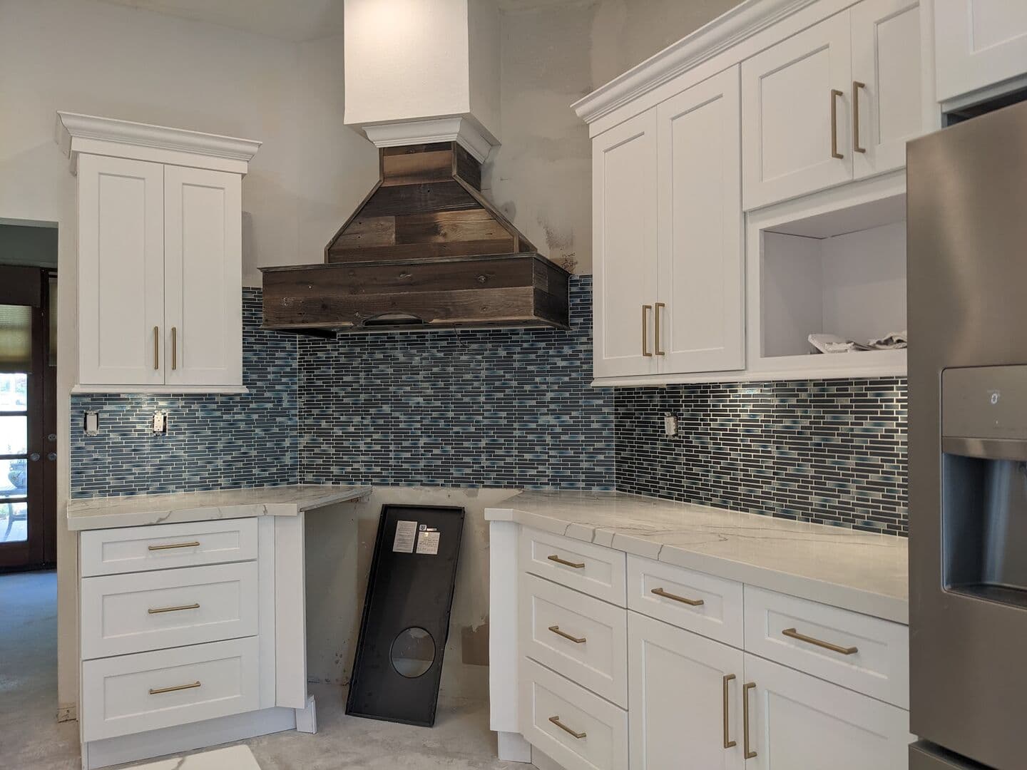 White kitchen with a blue glass mosaic backsplash, quartz counters and a wood range hood
