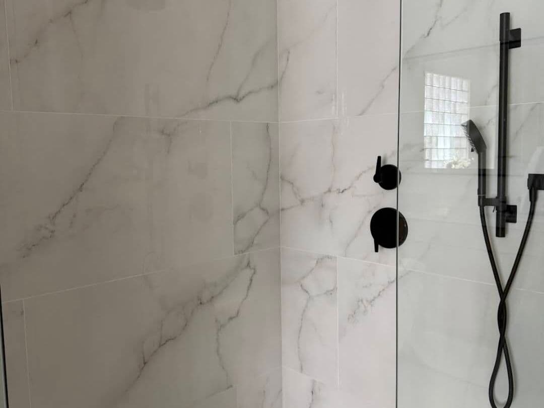 Calacatta marble-look shower with matte black rain head and hand shower and a glass block window