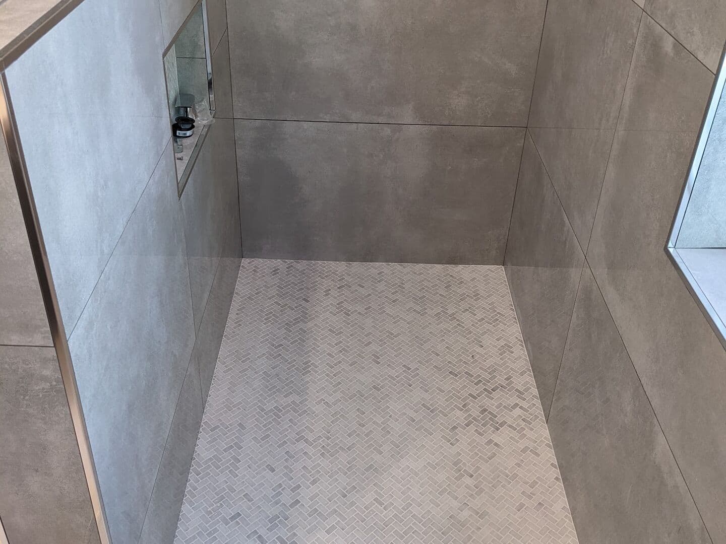 Concrete-look porcelain shower with a tiled bench, recessed niche and white marble mosaic floor