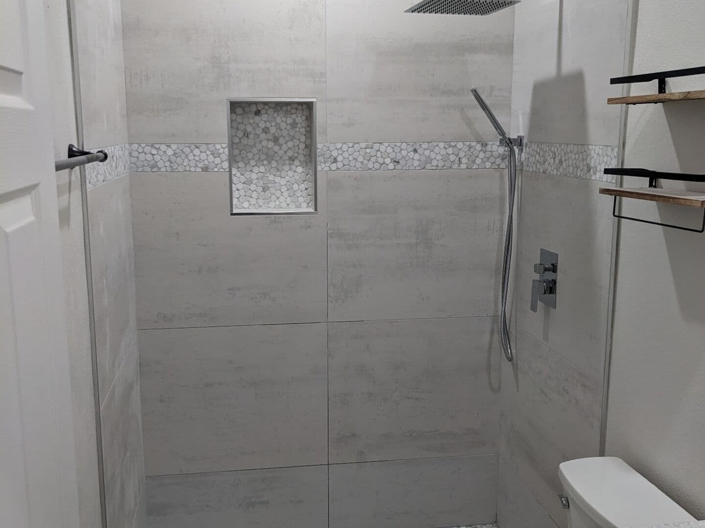 Concrete-look porcelain shower with a pebble floor and recessed niche