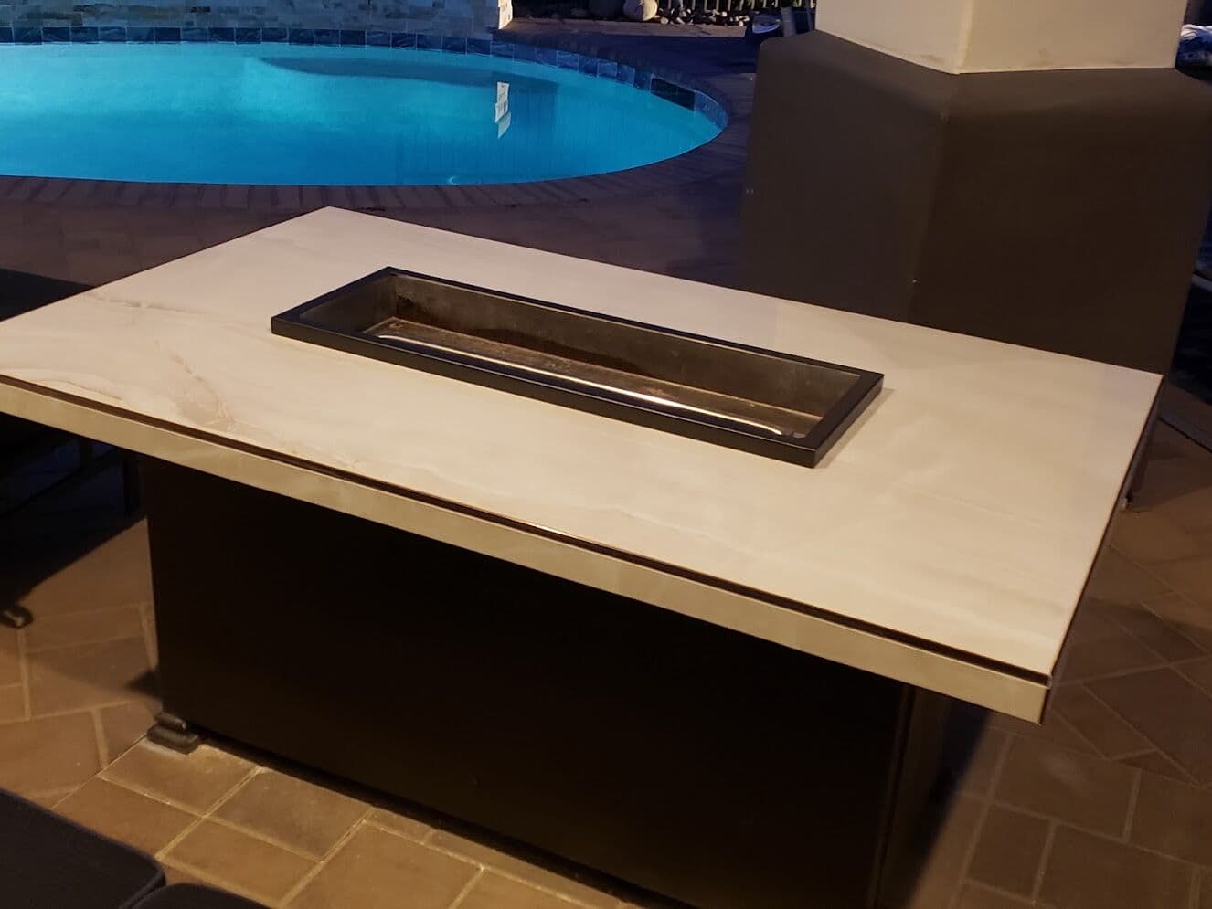 Outdoor fire pit table finished in tile beside a pool