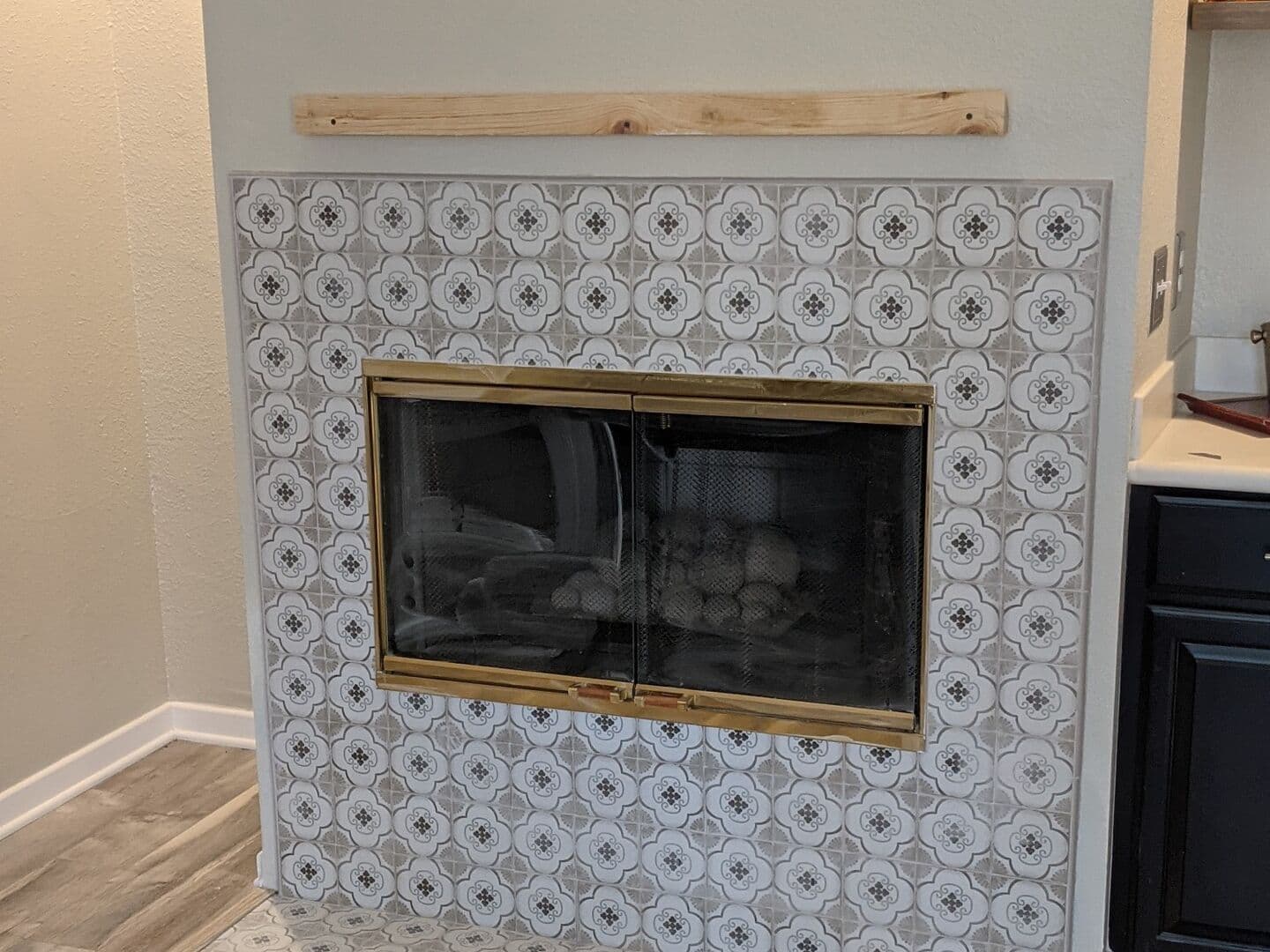 Fireplace surround and hearth tiled in grey-and-white patterned porcelain under a wood mantel