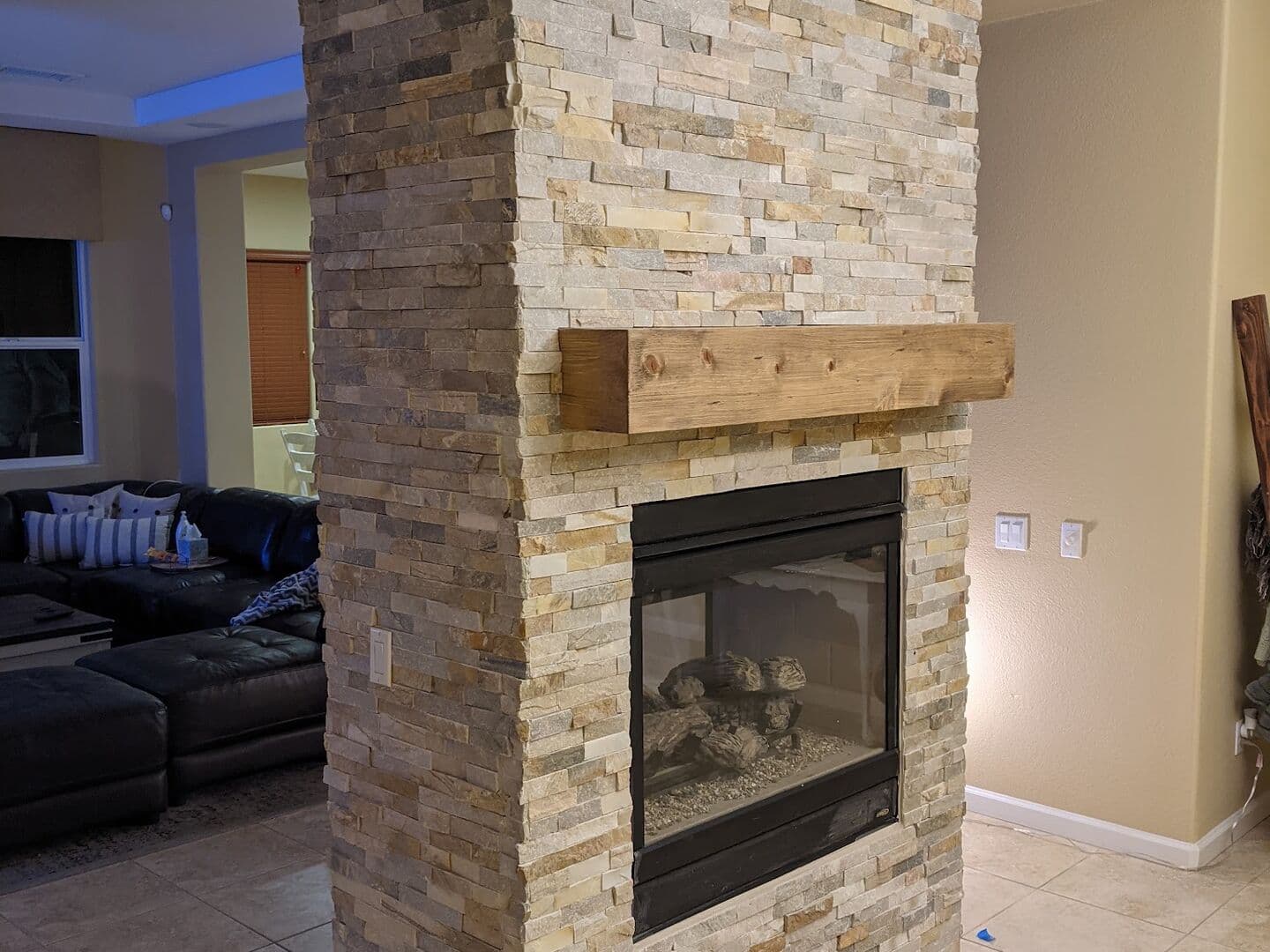 After: the same fireplace column wrapped floor to ceiling in stacked stone ledger panels with a rough-sawn wood mantel