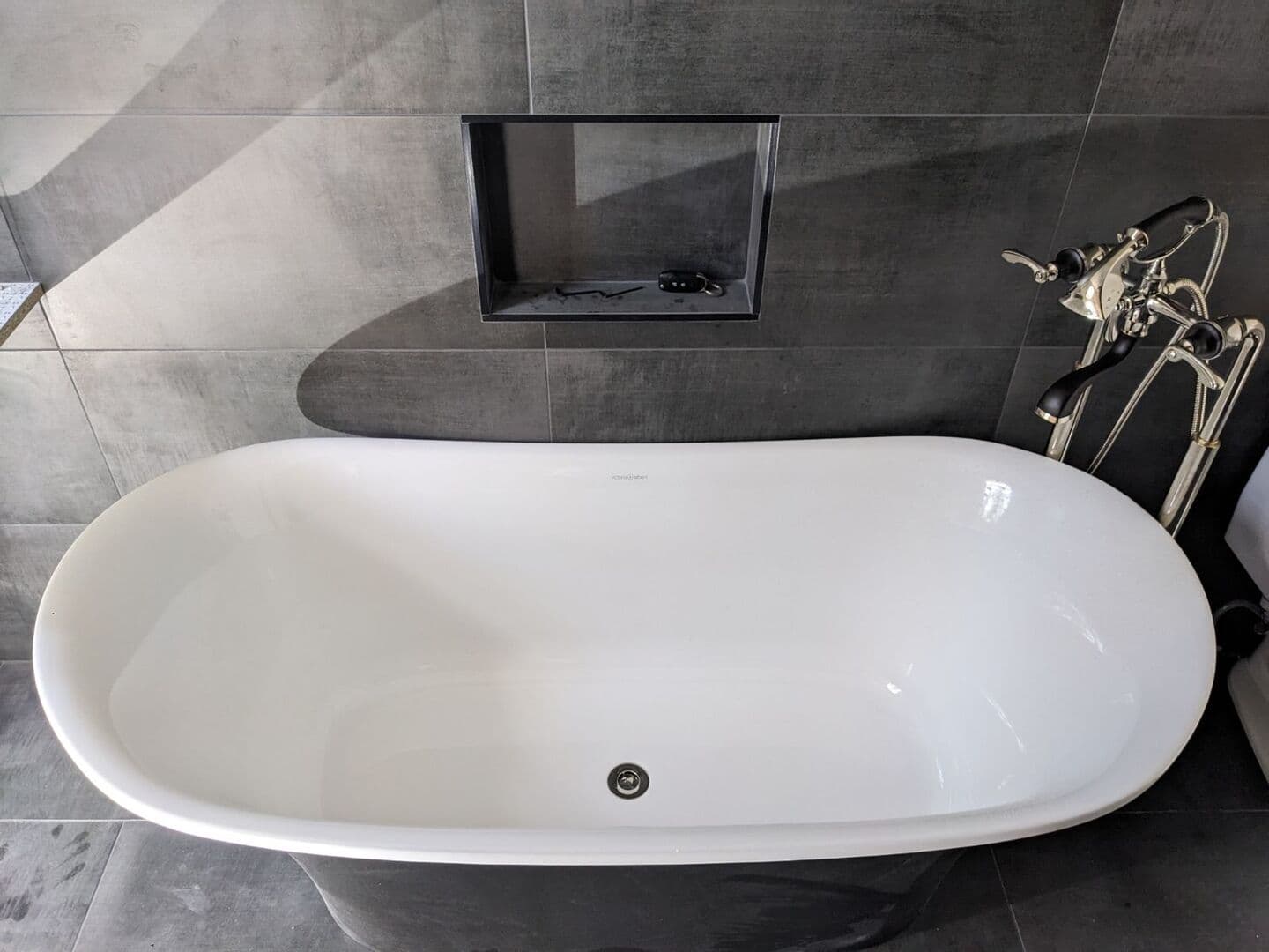 Freestanding tub against a dark grey large-format porcelain wall with a recessed niche
