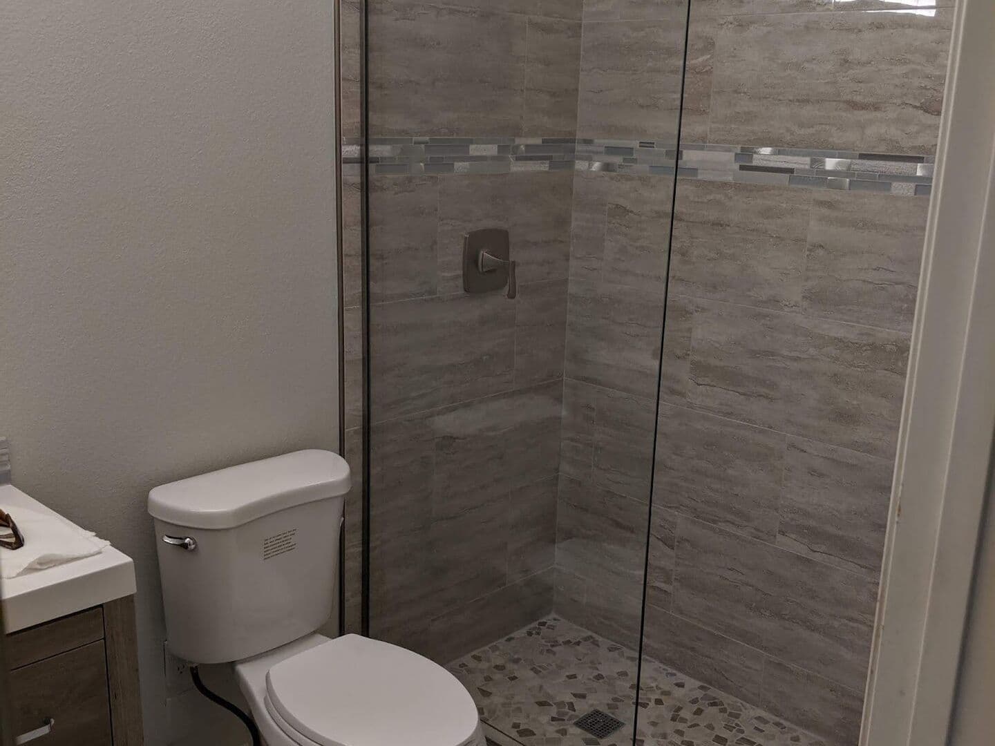 After: new grey vanity, tile floor and a walk-in shower in wood-look porcelain with a glass mosaic band, pebble floor and frameless glass