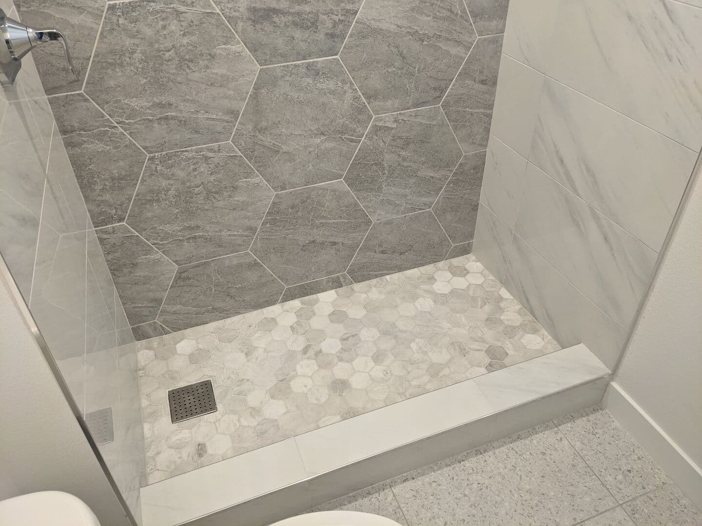 Shower with grey hexagon wall tile, white marble-look surround, hex mosaic floor and a tiled bench