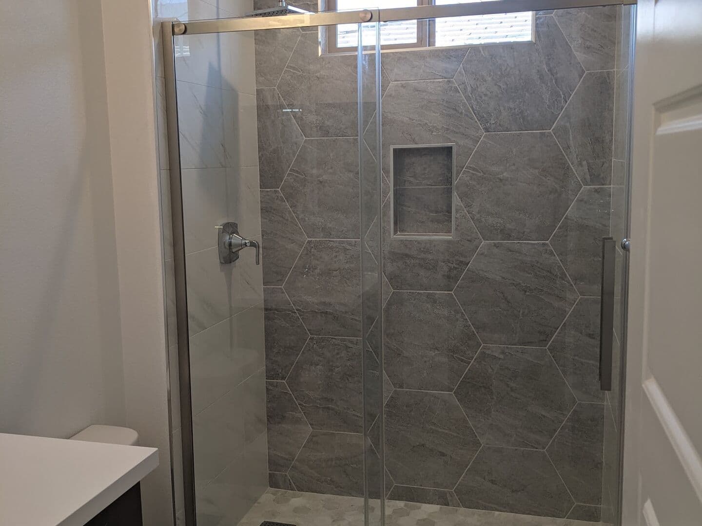 Bathroom with a hexagon-tiled walk-in shower behind a frameless sliding glass door