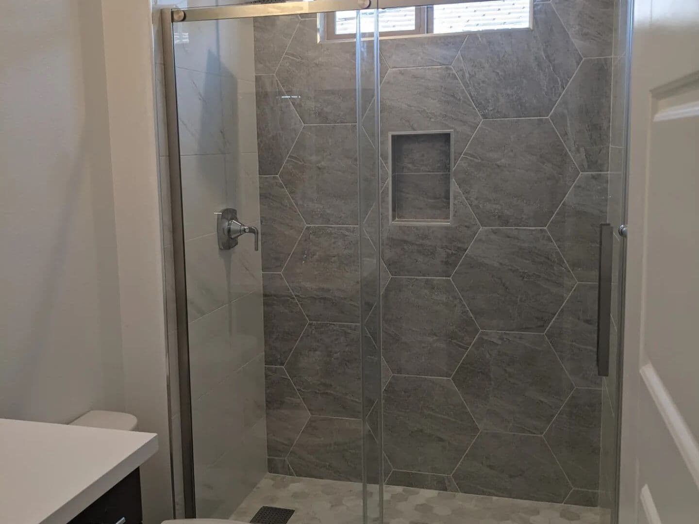 Grey hexagon-tiled shower behind a frameless sliding glass door