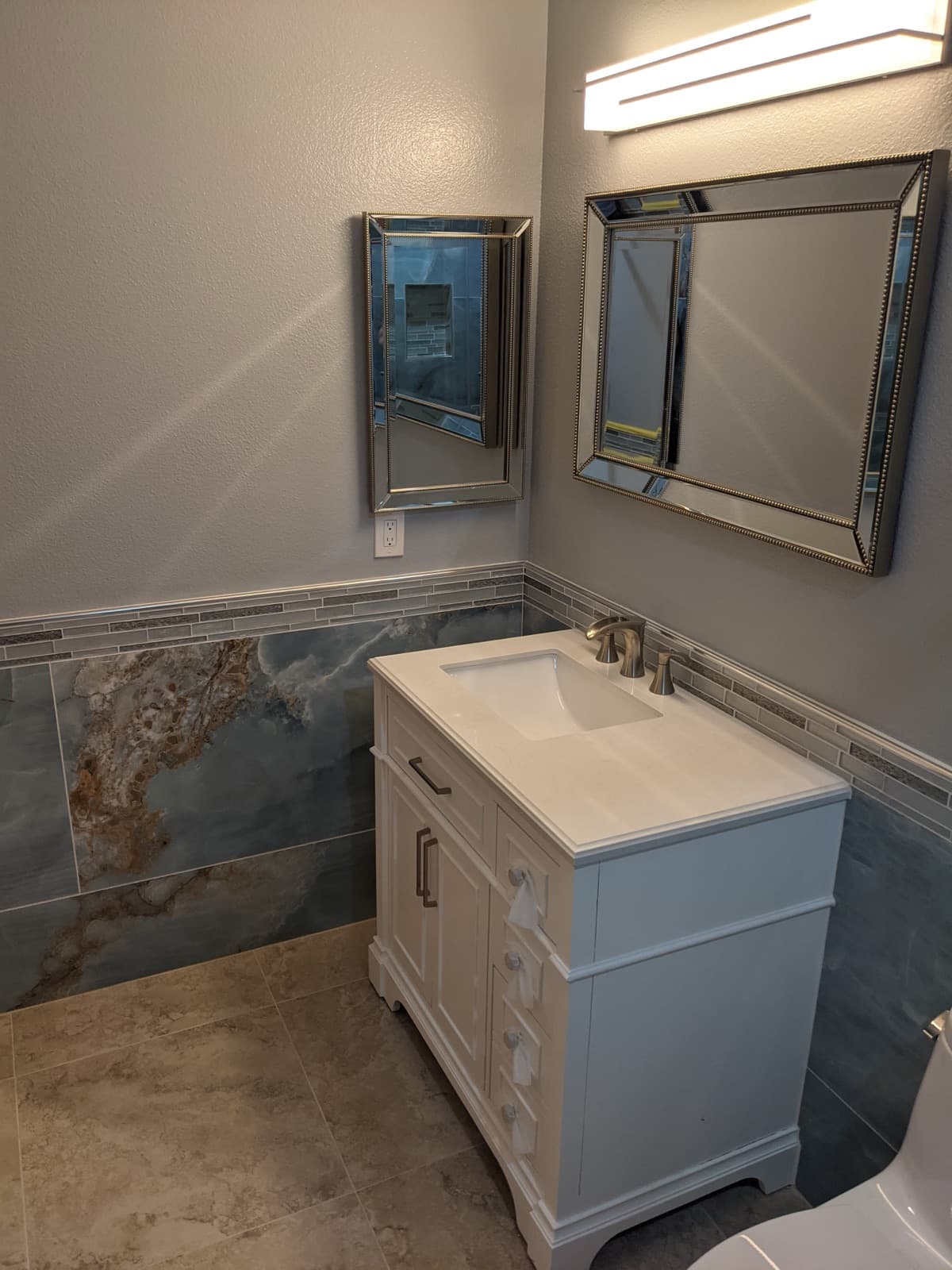 Powder room with large-format blue porcelain wainscot, a glass mosaic border and stone-look porcelain floor