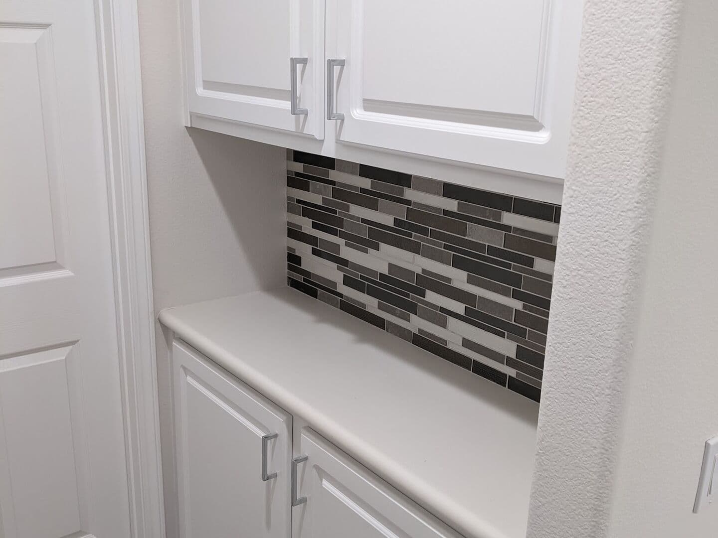 Laundry nook with a glass mosaic backsplash and white cabinets