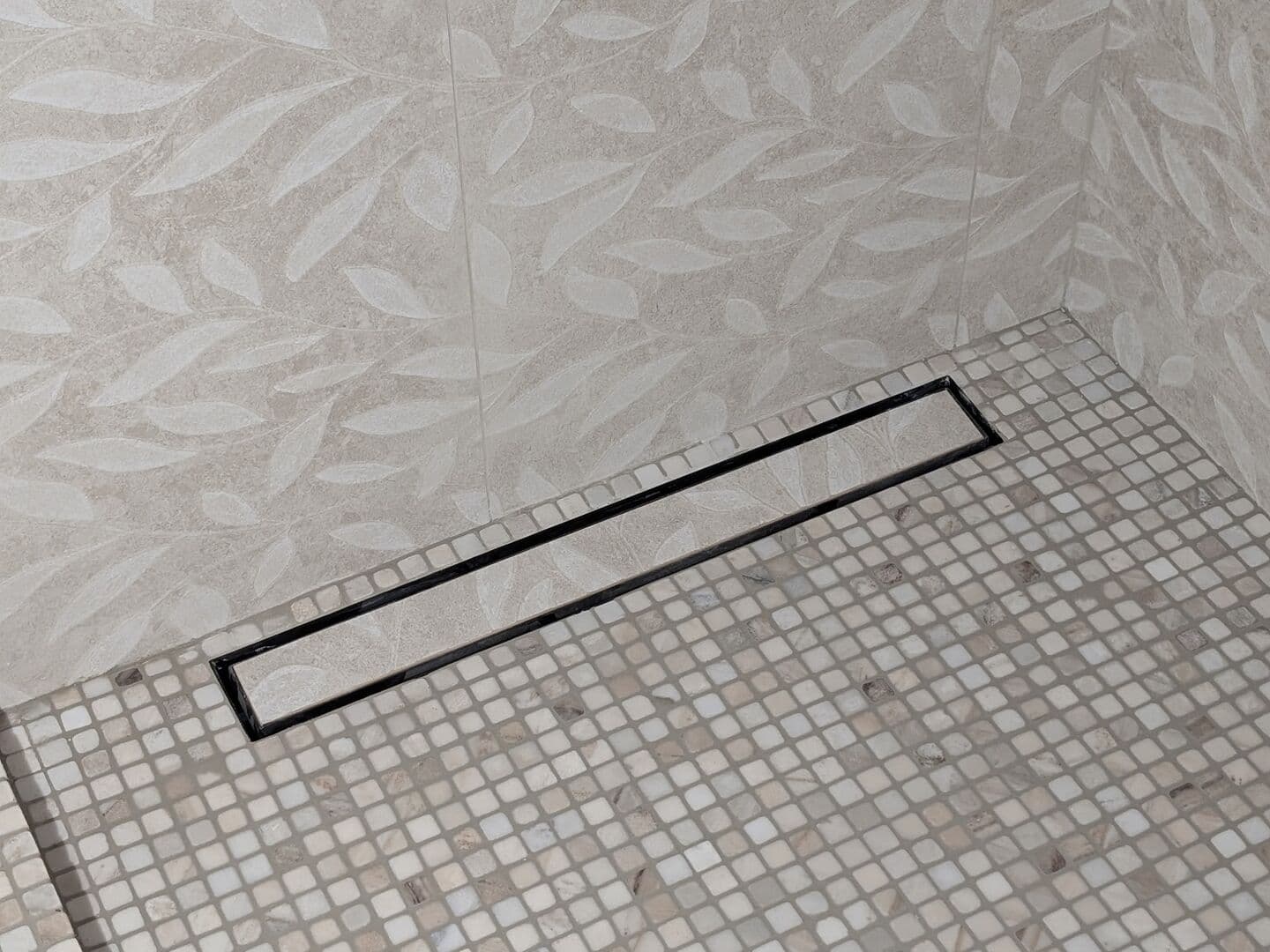 Shower with leaf-pattern porcelain walls and a stone mosaic floor with a linear drain