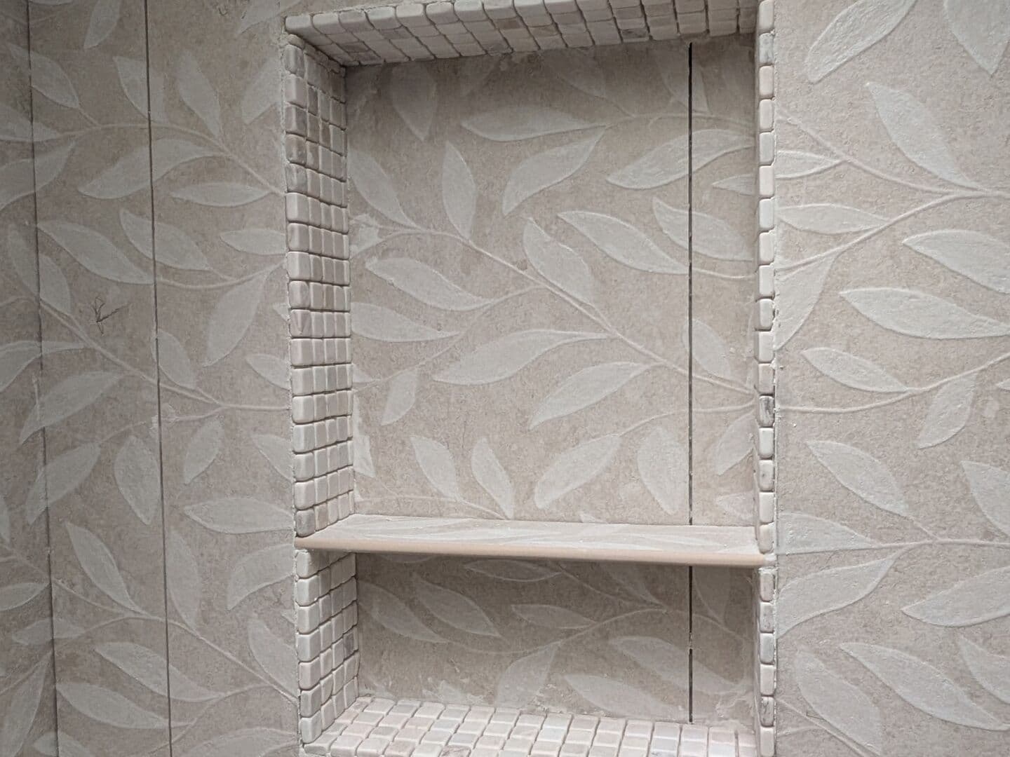 Recessed shower niche with a shelf set into leaf-pattern porcelain tile