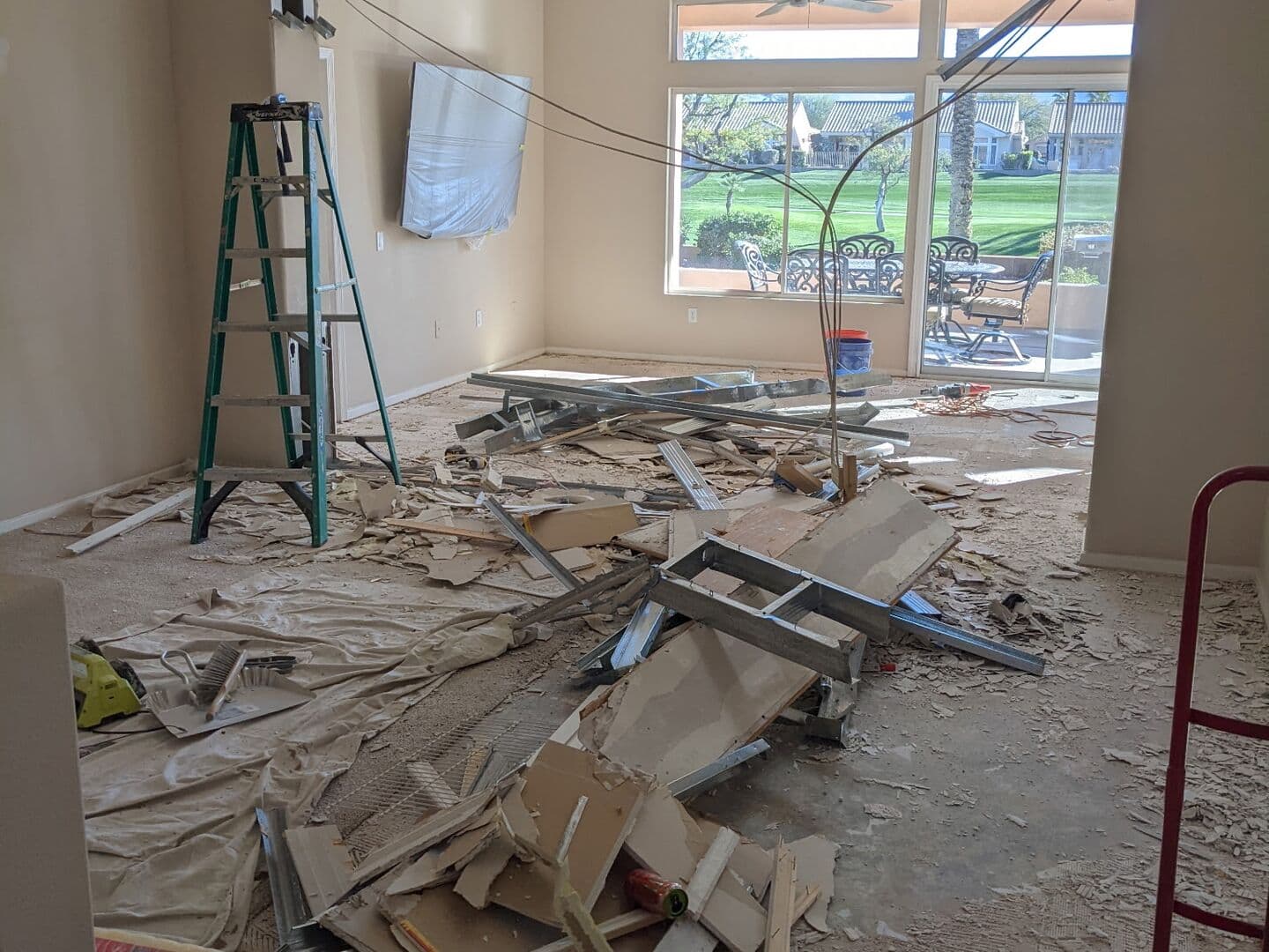 Before: living room stripped to the slab during the remodel, with debris on the floor and a ladder by the window