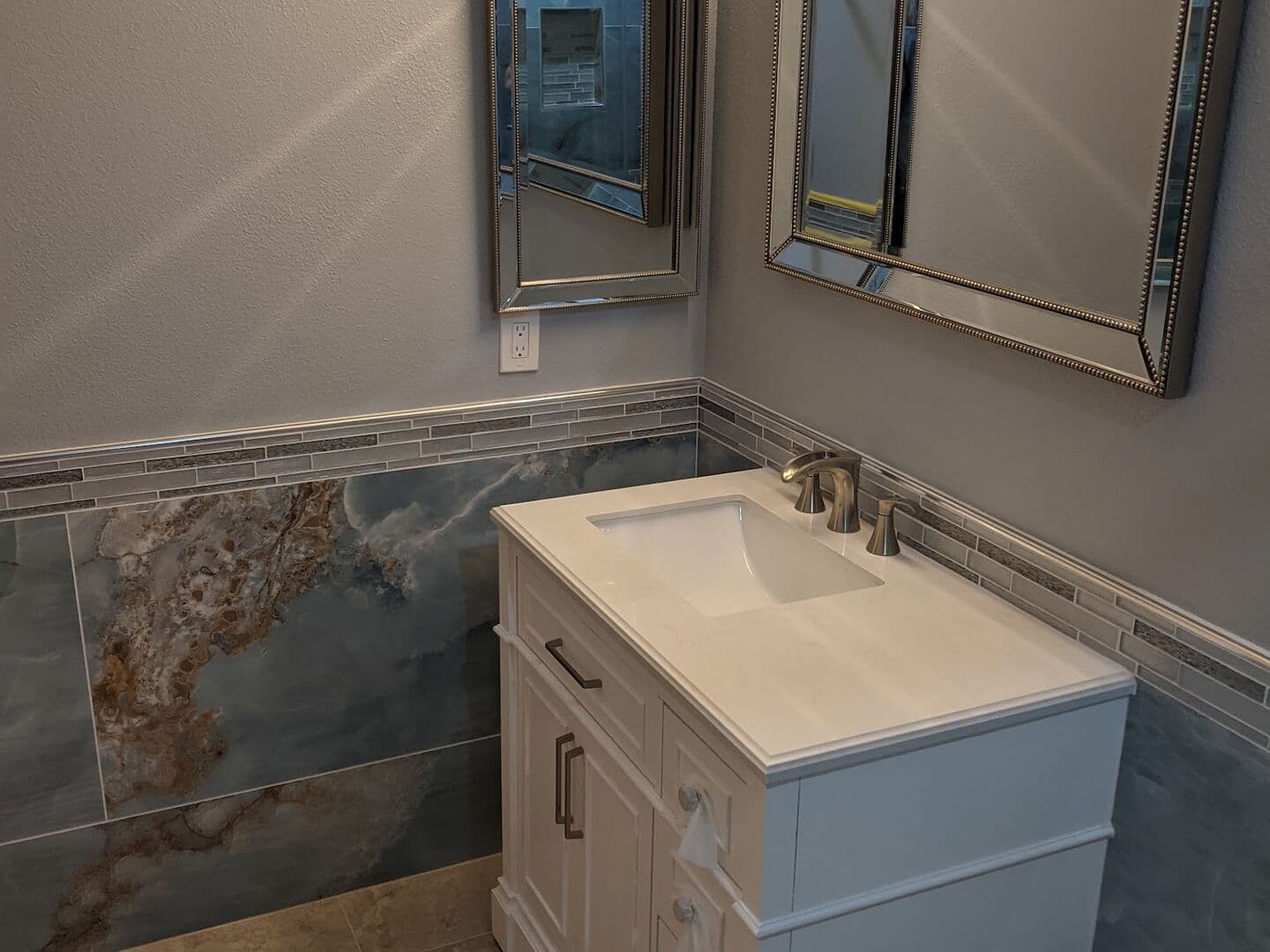 Powder room with onyx-look large-format porcelain wainscot, a glass mosaic border and stone-look floor