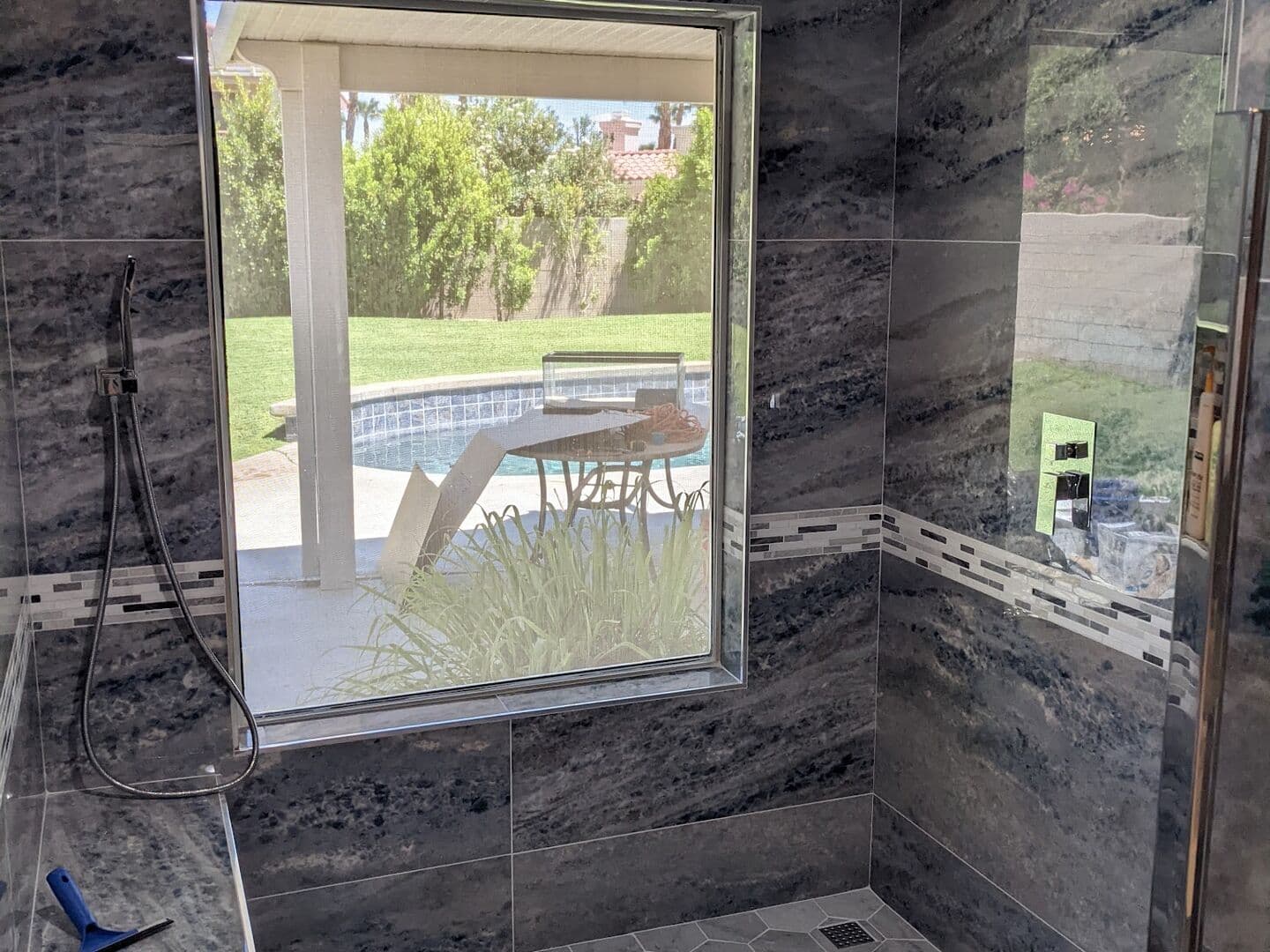 After: walk-in shower in blue onyx-look large-format porcelain with a glass mosaic band, built-in bench, marble hex floor and the window kept as a feature