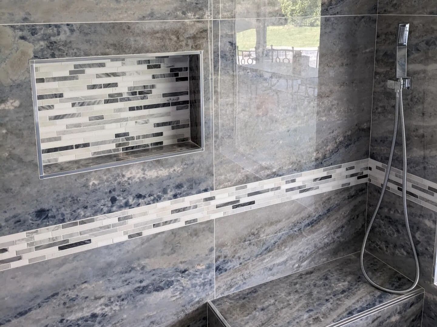 Recessed niche with a glass mosaic band and a tiled bench in blue onyx-look porcelain