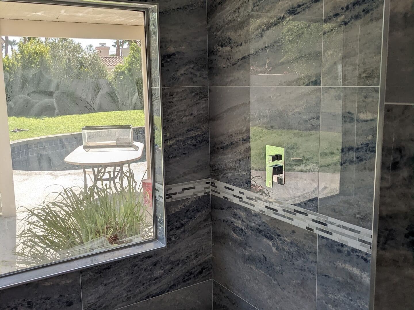 Walk-in shower in blue onyx-look large-format porcelain with a picture window, glass mosaic band and ceiling-mounted rain head