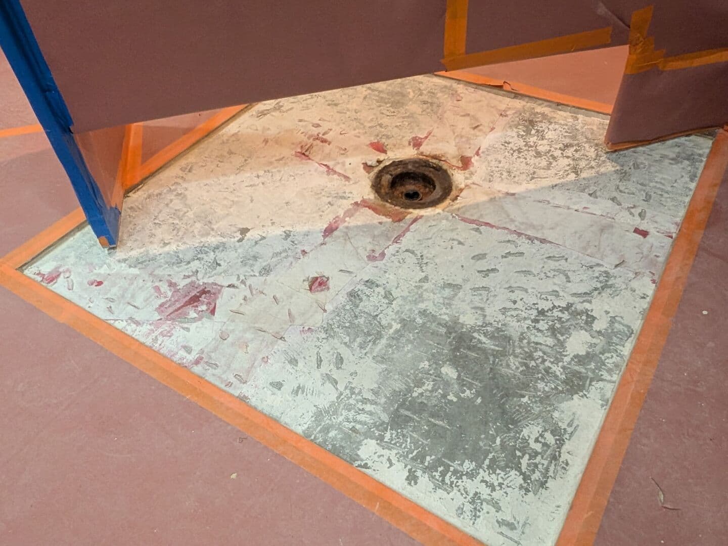 Before: commercial restroom floor cut open around a failed drain and masked off for the repair