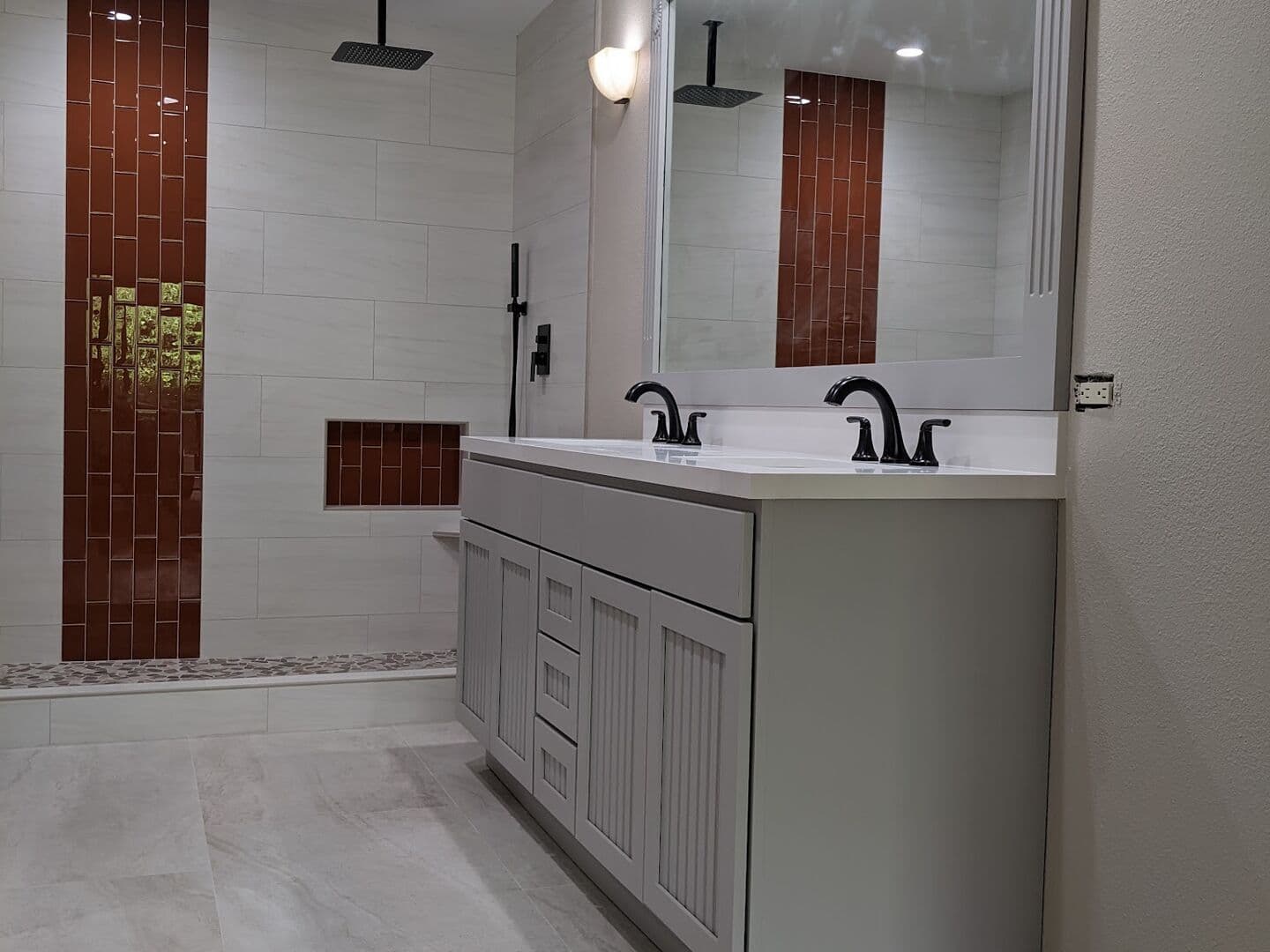 Master bath with a grey double vanity, white large-format floor and an open shower with a rust glass accent