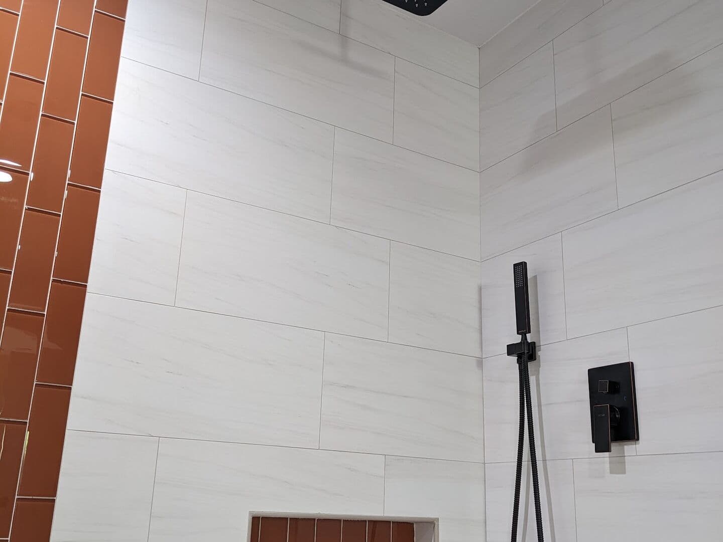 Walk-in shower in white large-format tile with a rust glass vertical accent stripe and black rain head
