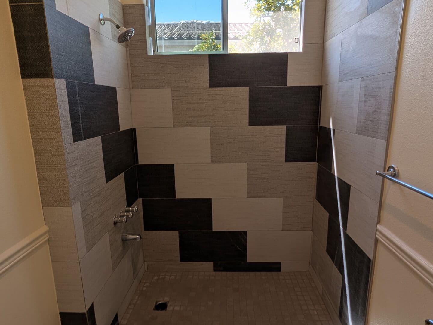 Shower with a staggered black, grey and cream tile pattern and a window