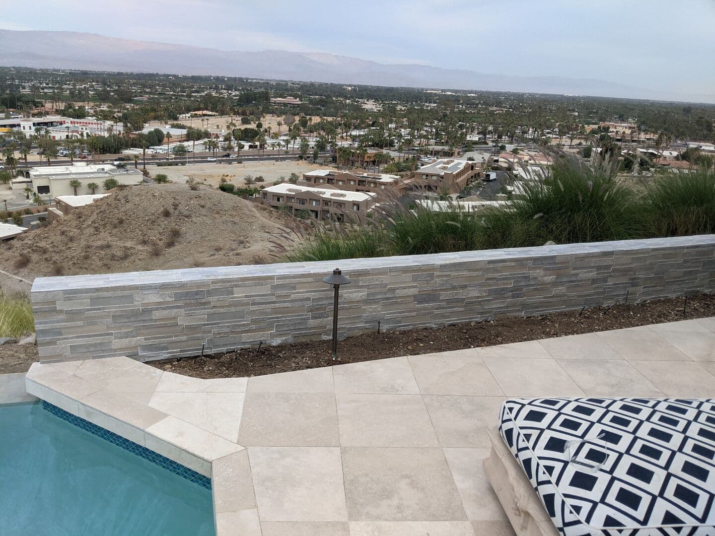 Stacked stone retaining wall beside a pool and travertine patio