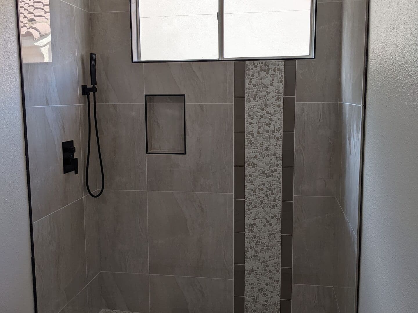 Walk-in shower with large-format grey tile, a vertical mosaic accent stripe, matte black fixtures and a frameless glass panel