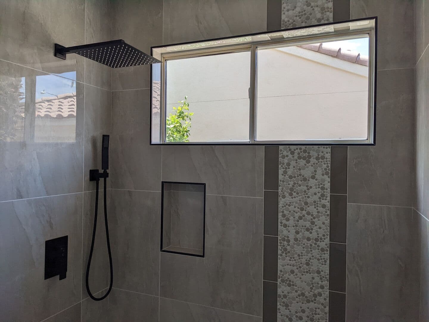 Shower with a window, recessed niche, black rain head and hand shower on large-format grey tile
