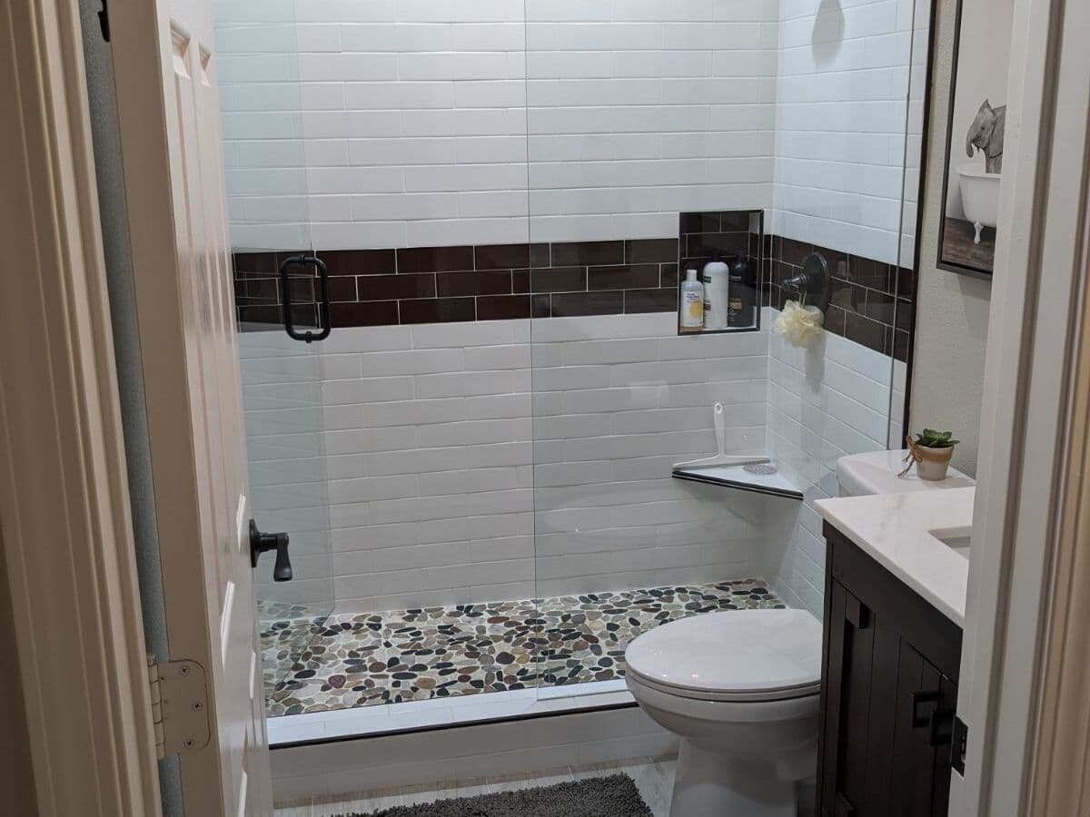 Shower in white subway tile with a dark accent band and a pebble floor