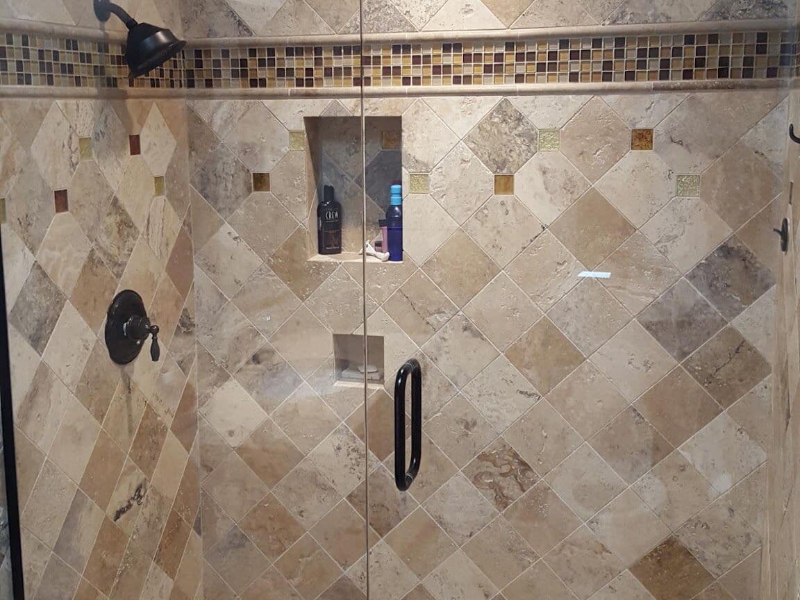Travertine shower set on the diagonal with a glass mosaic border, niche and frameless glass door