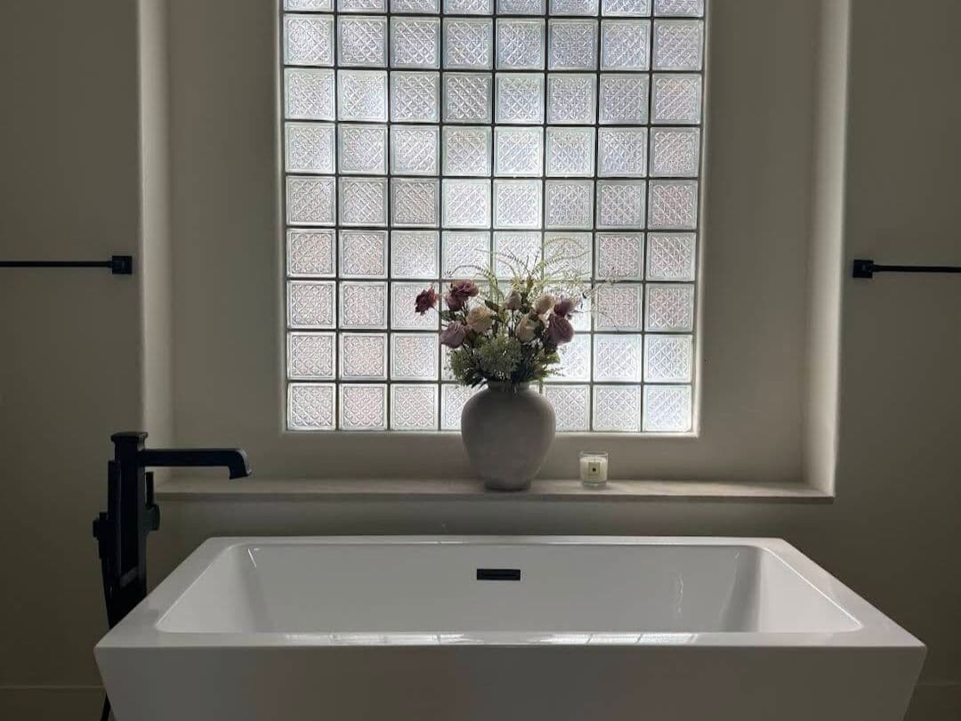 Freestanding tub under a glass block window with a matte black floor-mounted filler