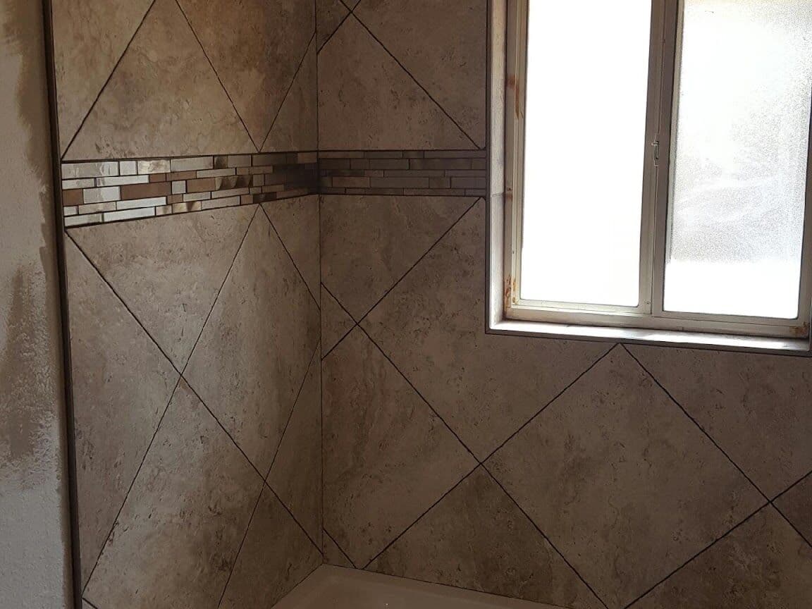 Tub surround tiled on the diagonal with a glass mosaic border around the window